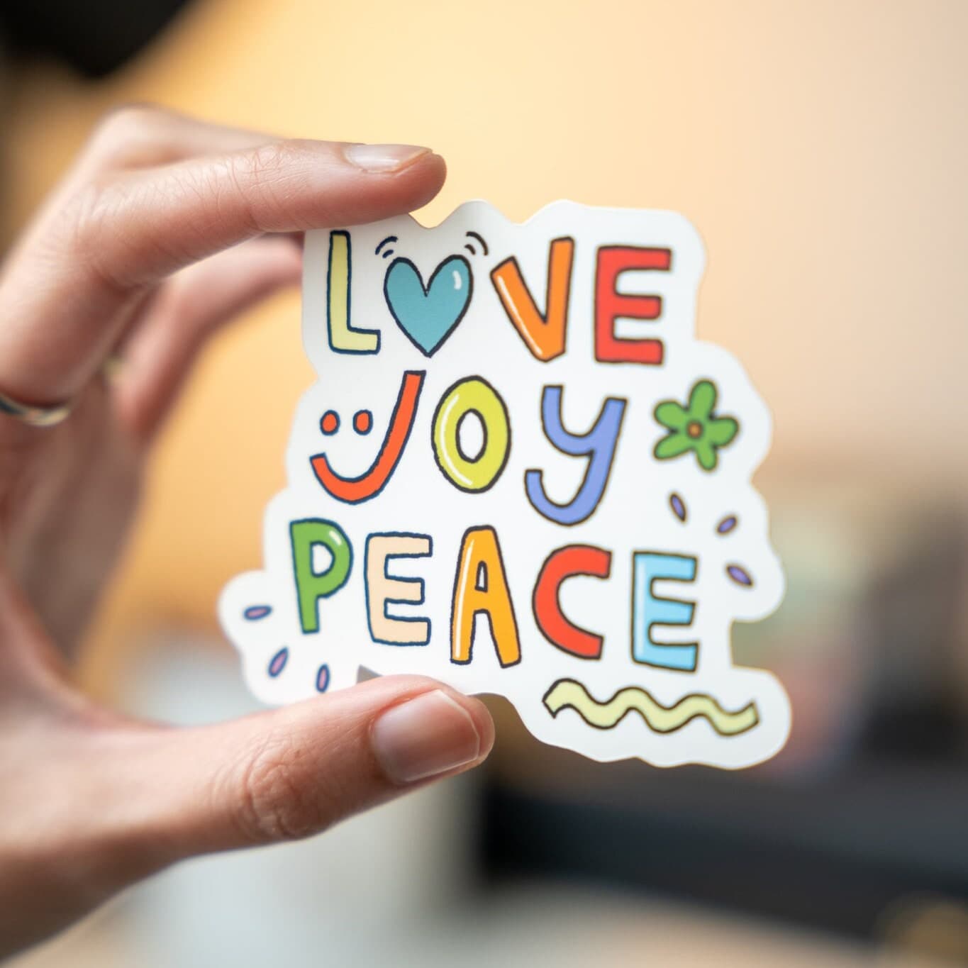 Hand holding a colorful Love Joy Peace vinyl sticker